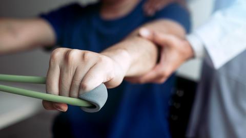 Asian male physical therapist descent working with patient doing stretching exercise with a flexible exercise band in clinic room.