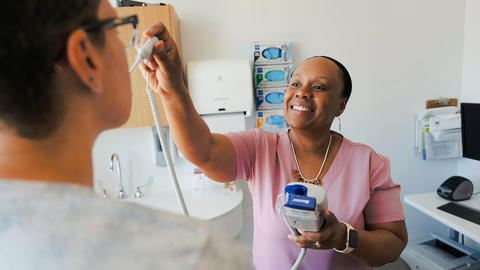 A health assistant is taking the temperature of a patient in the Urgent Care department of HUHS