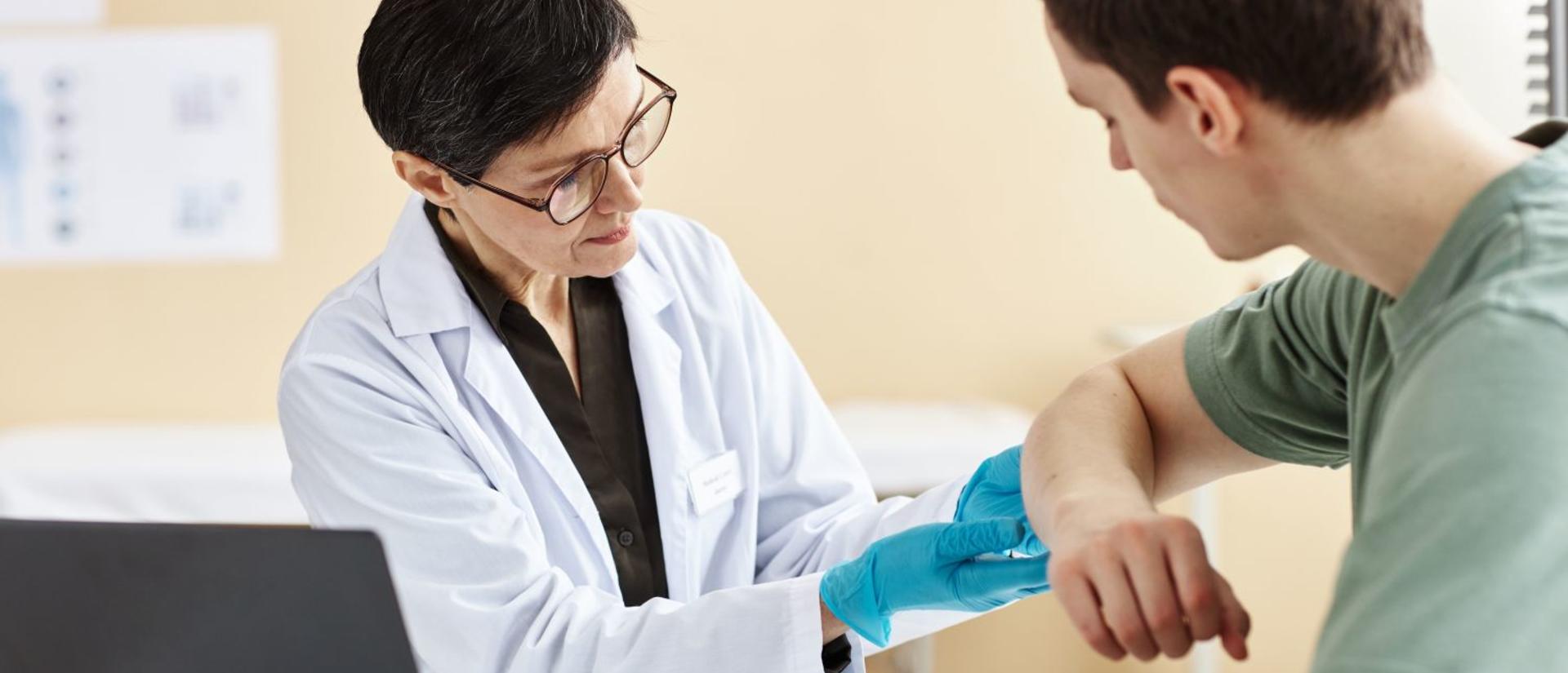 Portrait of mature female doctor inspecting patient with skin rash during consultation in dermatology clinic