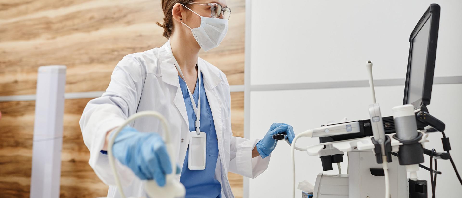 Side view portrait of female doctor using ultrasound machine and wearing mask while examining pregnant woman in clinic