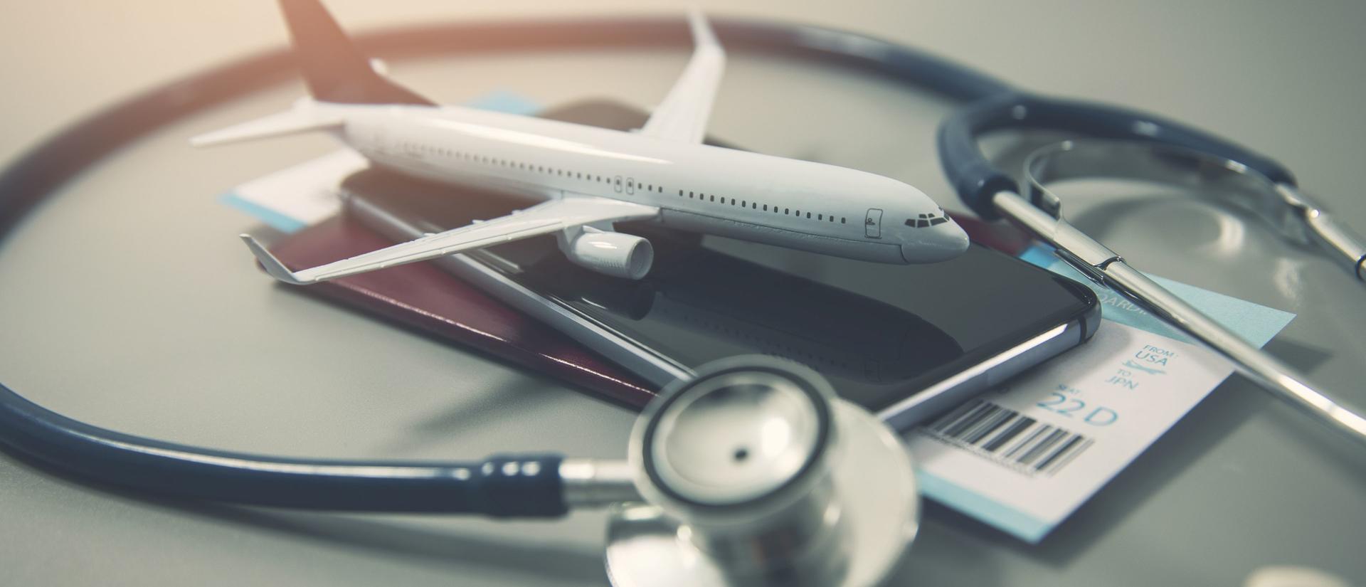 A model airplane on a smartphone, surrounded by a stethoscope and a partially visible boarding pass, symbolizing travel and healthcare.