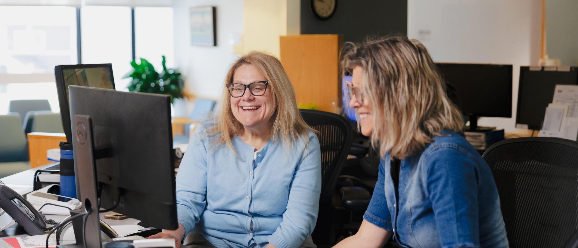 HUHS primary care staff sitting together at the front desk, looking at a computer screen, and laughing