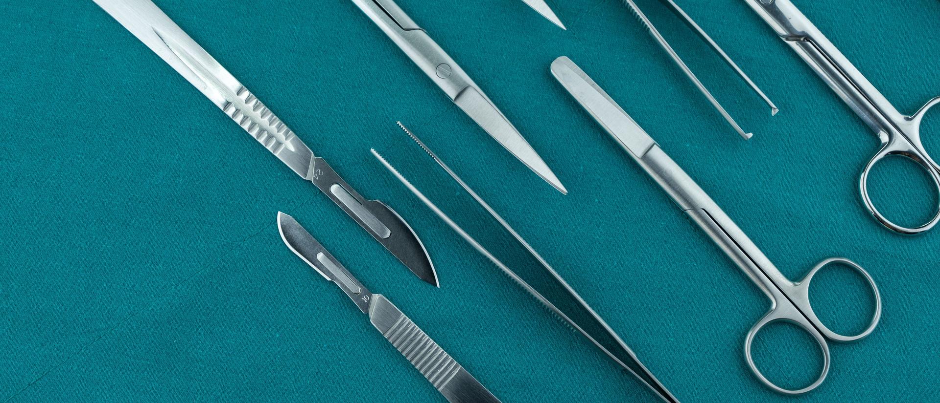 Basic surgical instrument scalpel forceps tweezers scissors spread on surgical green drape fabric